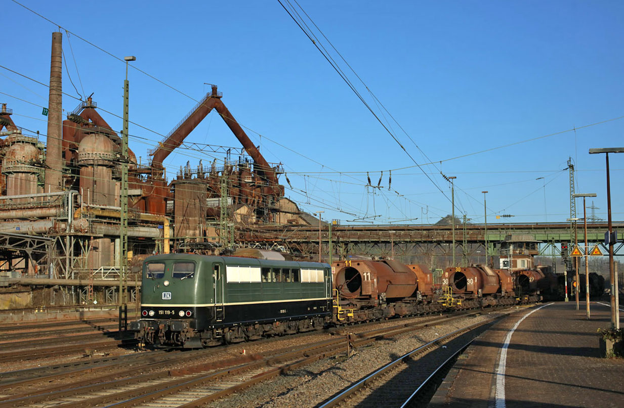 On 29 March 2021 Saar Rail used Bayernbahn 151 119 (rented via Leipziger Dampf KulTour) to haul liquid iron train 91305 from Dillingen Hochofen to Vlklingen, here seen at arrival at Vlklingen in front of the Unesco World Heratige Site of Vlklinger Htte (an old iron factory).